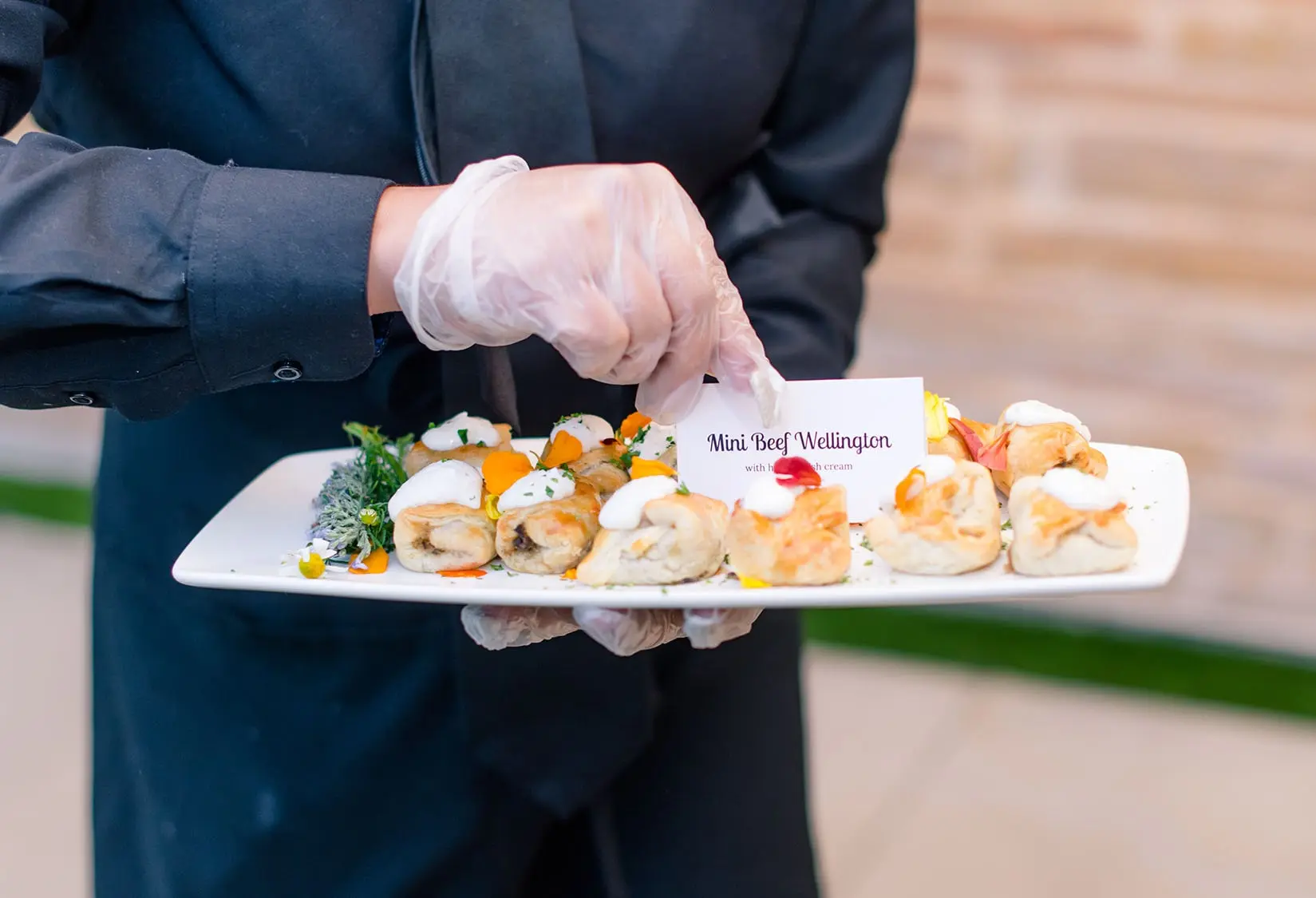 Server presenting a tray of mini Beef Wellington hors d'oeuvres garnished with herbs and edible flowers at The Red Berry Estate event.
Photo: T Walker Photography