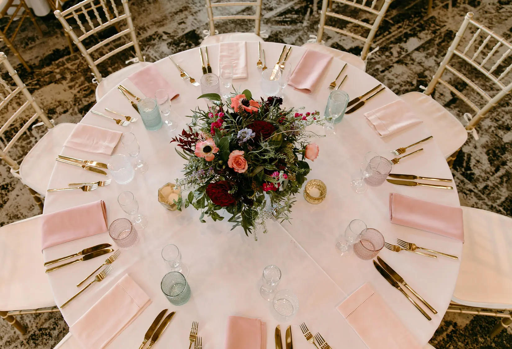 Wedding reception round table set with blush napkins, gold flatware, and a vibrant floral centerpiece at the Lakeside Ballroom at The Red Berry Estate.
Photo: Jessie Schultz Photography