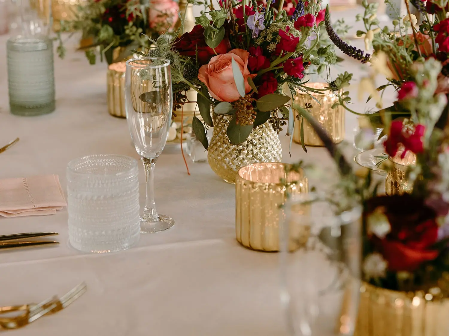 Detail shot of romantic floral arrangements, votive candles, and champagne flutes on a long reception table at the Lakeside Ballroom at The Red Berry Estate.
Photo: Jessie Schultz Photography