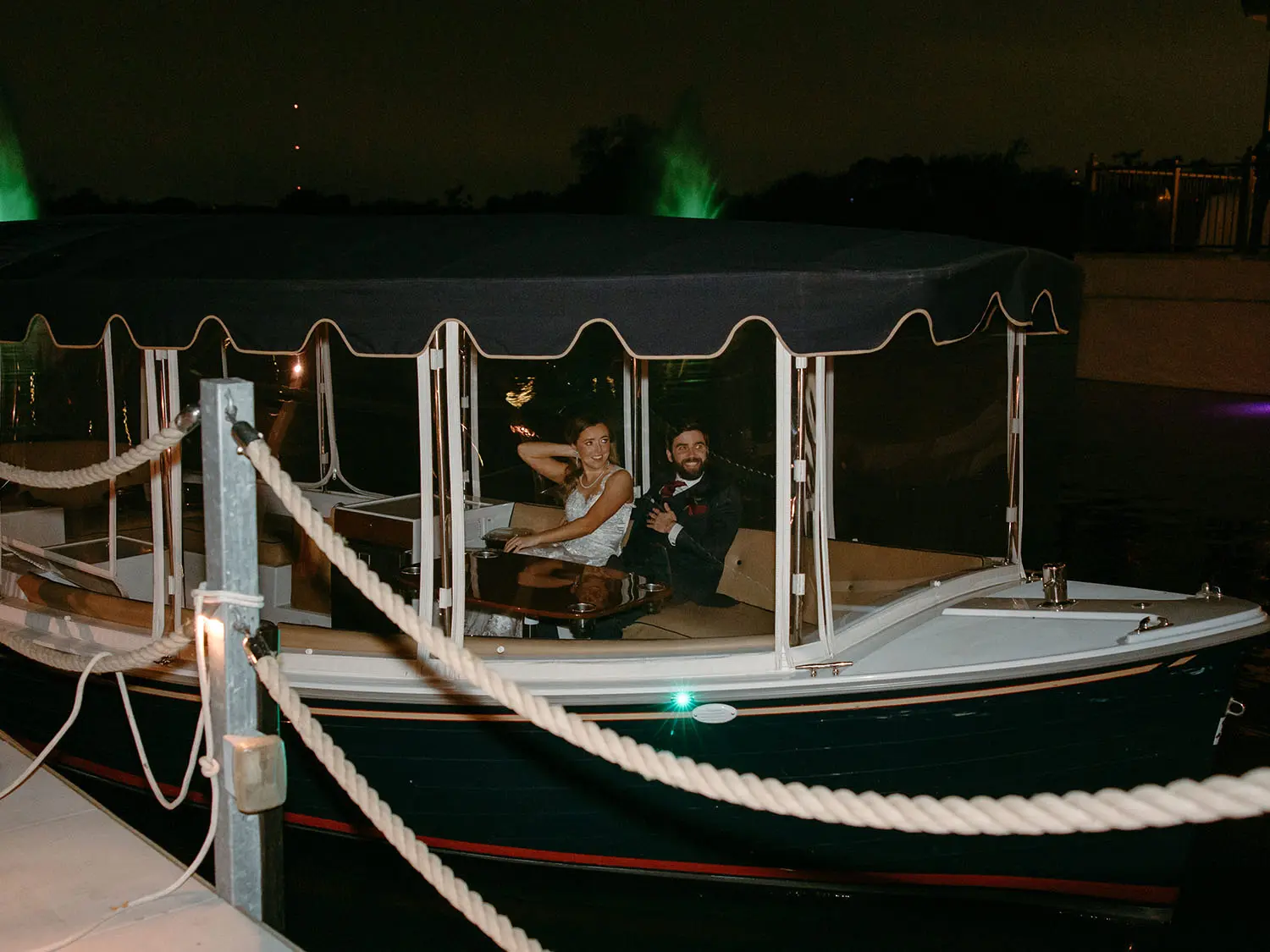 Bride and groom departing the wedding reception in a covered boat on the lake at The Red Berry Estate under evening lights.
Photo: Jessie Schultz Photography