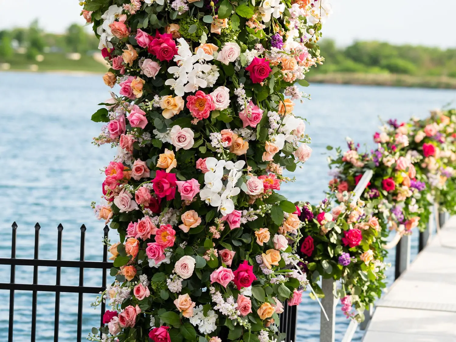 Vibrant floral column bursting with roses, orchids, and greenery lining the waterside wedding aisle at The Red Berry Estate.
Credit: Parish Photography