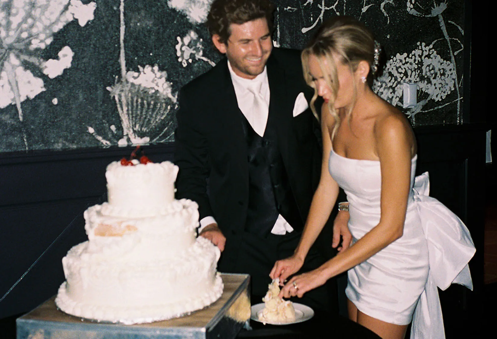 Groom looking at bride cutting wedding cake, on film photography