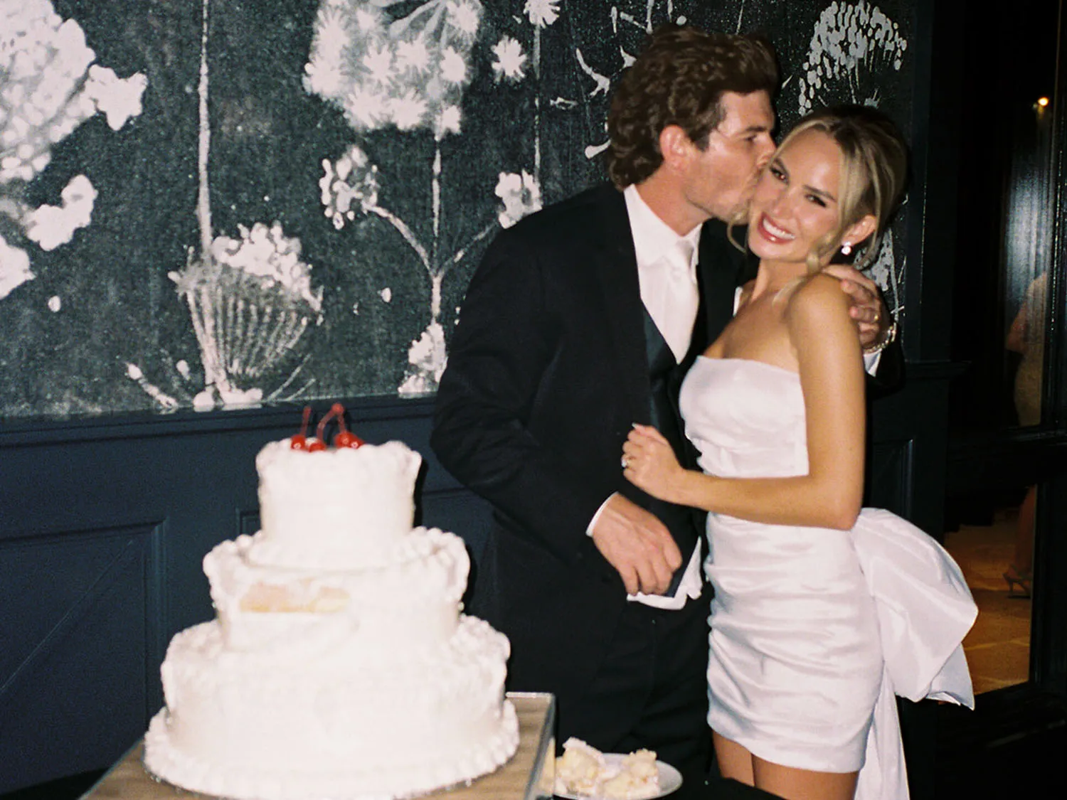 Groom kissing bride on cheek before wedding cake, on film photography