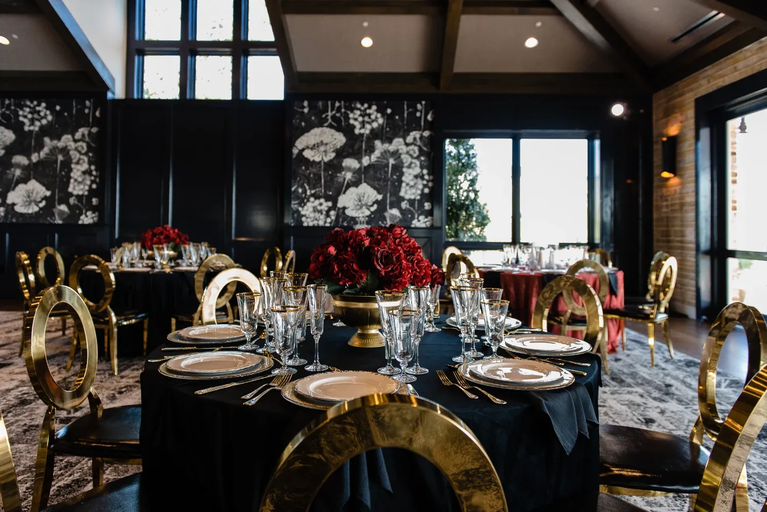 Elegant indoor event space at The Red Berry Estate featuring round tables with black linens, gold chairs, and formal table settings.